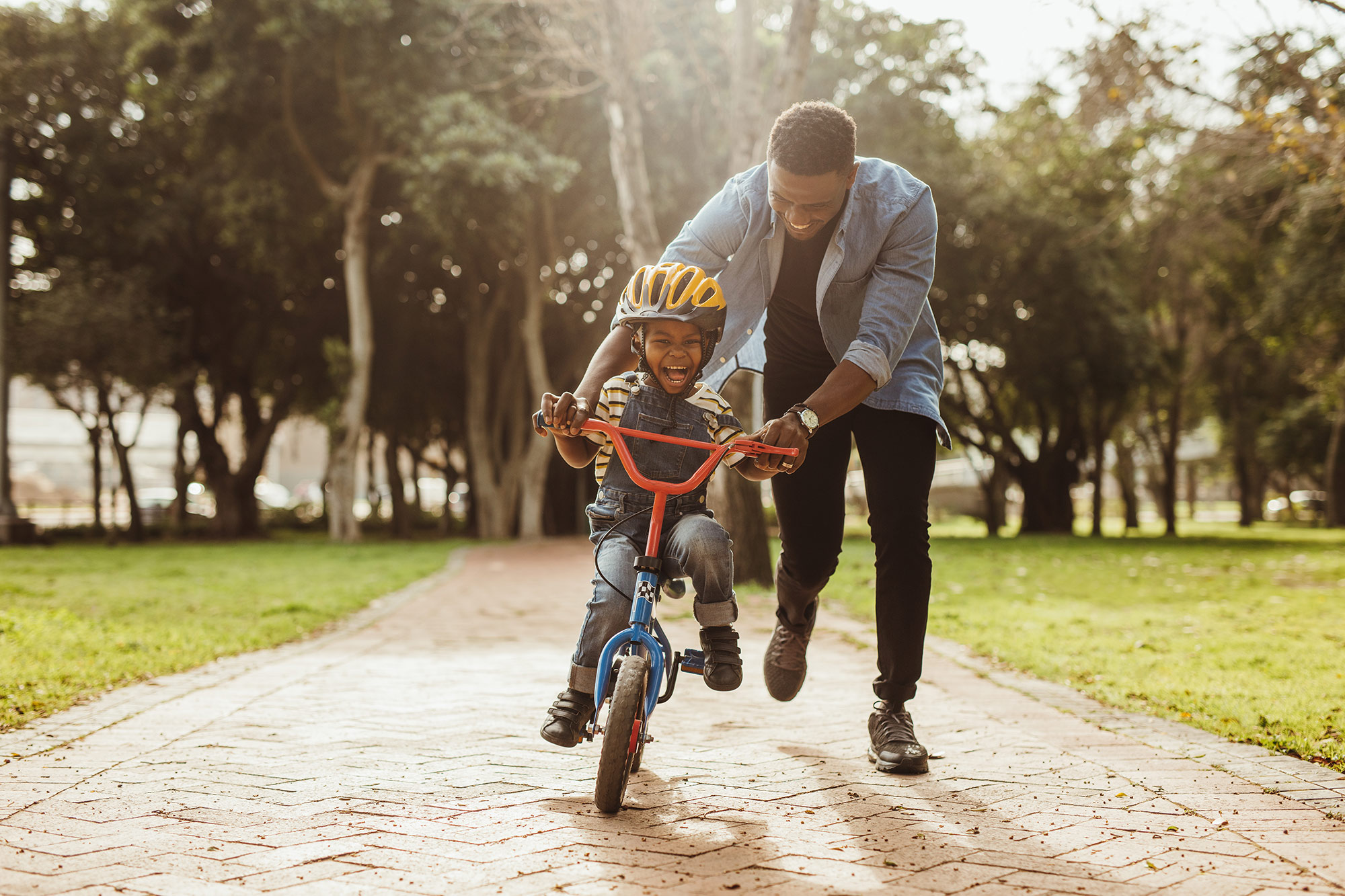 Father pushes young son on bicycle