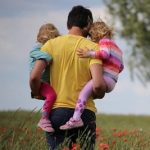 A man holds two little girls while walking through a field of flowers